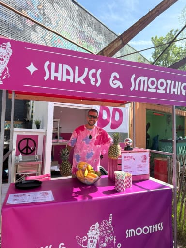 Een verkoper met fruit achter een kraam met shakes en smoothies